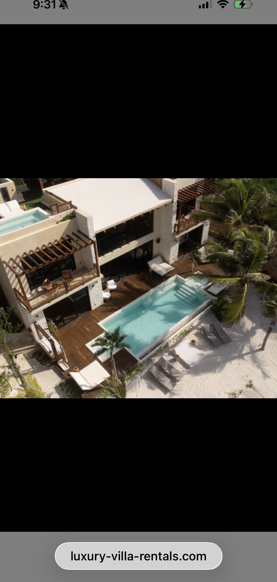 Aerial view of the villa: a white modern structure with a long lap pool on a teak deck, surrounded by palm trees, with white sand beach beyond.