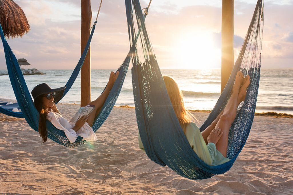 Two people relaxing in hammocks on the beach at sunrise at Ventus at Marina El Cid in the Riviera Maya